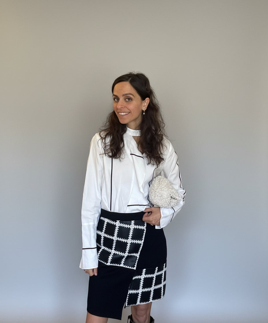 Woman in a white blouse and black and white checkered skirt standing in a room with a wooden door and tiled wall.