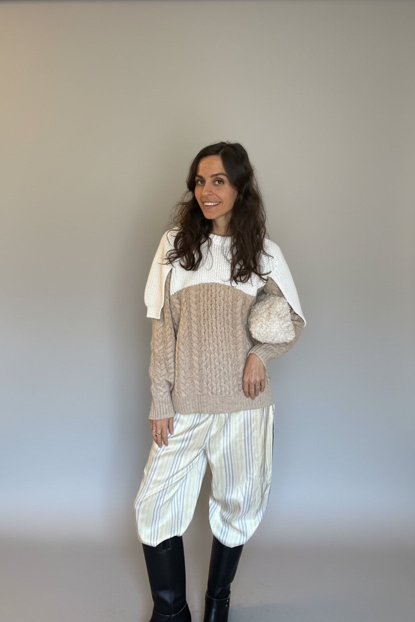 Woman wearing a beige and white outfit standing against a wall.